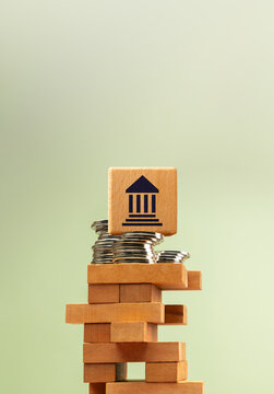 Wooden government bank symbol stacked on unstable blocks with coins, economic finance uncertainty
