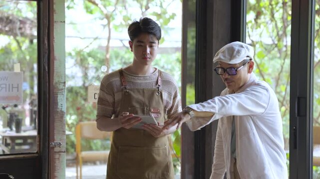 Family small business, senior cafe owner placing hiring sign on glass door, recruitment and expanding team concept in local coffee shop and restaurant. Cafe owner teaching barista about work process