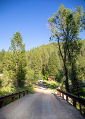 Obraz premium Perspective view of a dirt road bridge leading into a forested mountain valley