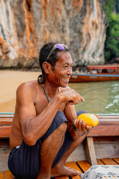 Smiling thai man eating mango on longtail boat