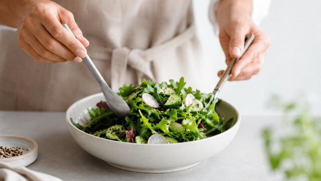 Person tossing fresh green salad in bowl
