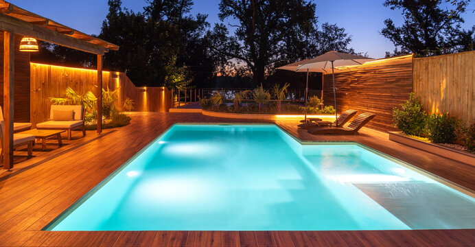 Pool and lounge area with soft night lighting and lush garden. Concept of luxury outdoor living and evening serenity