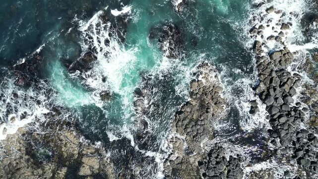 Aerial drone view of powerful ocean waves crashing against the rugged rocky coastline of Northern England, dramatic seascape with turquoise water, white sea foam, and natural coastal landscape