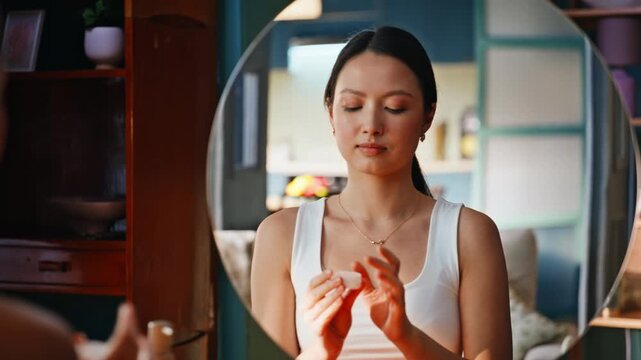 Asian woman applying face cream mirror. Closeup skincare beauty routine home.