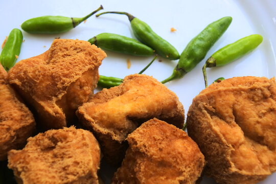 Close up of Tahu Sumedang, Indonesian traditional deep fried tofu served with fresh green bird's eye chilies on a white plate.