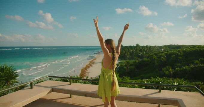Smiling woman raises arms at scenic viewpoint overlooking Playa Santa Fe beach in Tulum Mexico