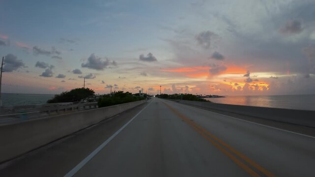 Driving a car on empty Overseas Highway bridge stretching over the water during a vibrant sunset in Florida, United States