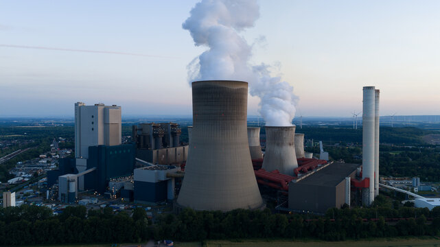 Aerial view of Kraftwerk Niederaussem with its large cooling towers emitting steam plumes, surrounded by lush greenery and industrial infrastructure in Bergheim, Nordrhein-Westfalen, Germany.