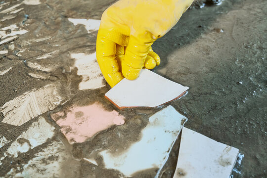 Hand in yellow rubber glove placing ceramic pieces into wet cement for mosaic. Upcycling old materials