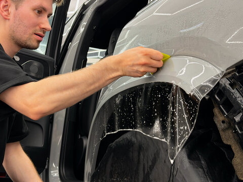 A car wrapping specialist applies a polyurethane film to the car. Detailer smoothes PPF. Car wrapping, detailing, tuning and styling. PPF protective film against chips and scratches. Protects the car.