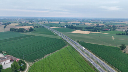 Aerial establishing shot showcasing the vast agricultural fields with prominent garlic crops growing in the Po Valley. A major highway connecting Monticelli d'Ongina to Cremona through Emilia Romagna © august.columbo