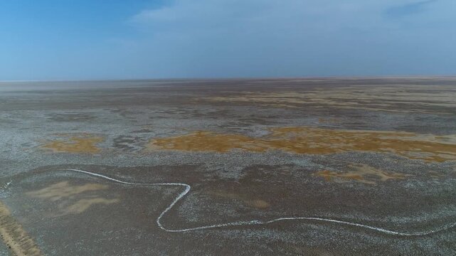 Professional drone shot captures winding paths through desert salt marsh with white and brown surface variations.