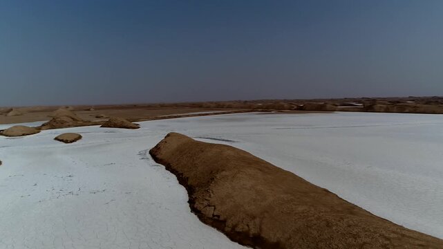 Dynamic drone shot reveals desert salt marsh with irregular white salt deposits and dark soil channels creating abstract patterns from above.