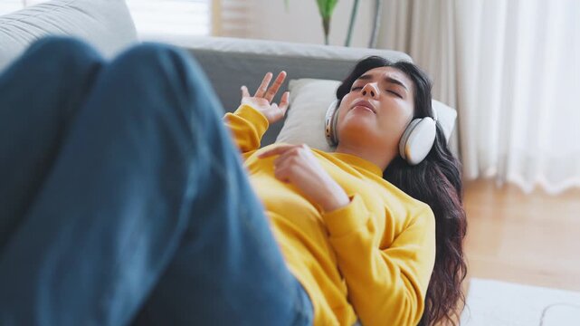 Portrait of Asian woman relaxing listening audio with headphones sitting on a couch at home