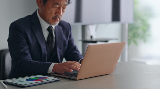 ノートパソコンとタブレットPCを使って作業する男性。ビジネス、デスクワーク、DX、仕事、オフィス