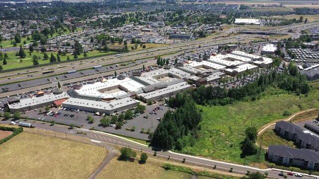 4K aerial drone footage of a busy outlet shopping center in Woodburn, Oregon, USA during the Juneteenth holiday with crowded parking lots, retail stores, and shoppers