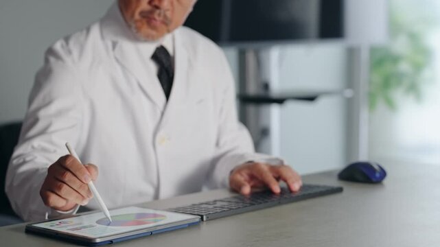 パソコンとタブレットPCを使って作業する白衣の男性。医師、科学者、研究者、DX、IT、技術者、仕事