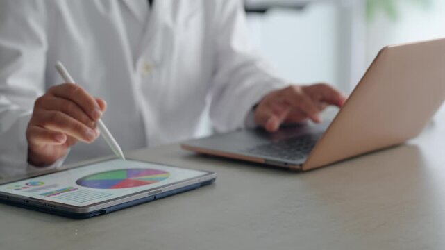 ノートパソコンとタブレットPCを使って作業する白衣の男性。医療、科学、研究、開発、経営、DX、AI