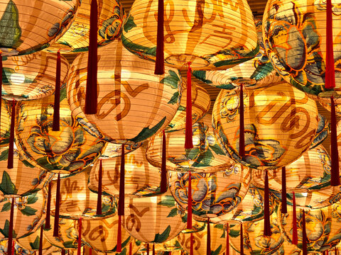 Gold lanterns fill ornate temple ceiling, warm glow casting patterned shadows, red tassels swinging