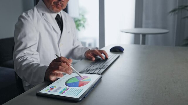 パソコンとタブレットPCを使って作業する白衣の男性。科学、研究、DX、IT、医療、医師、開発、データ