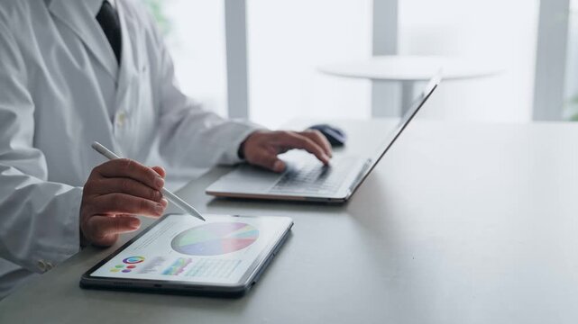 ノートパソコンとタブレットPCを使って作業する白衣の男性。科学、研究、医療、医師、実験、データ、分析