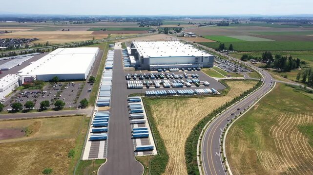 4K aerial drone footage of a major ecommerce fulfillment center and grocery distribution warehouses in Woodburn, Oregon, USA with numerous semi trucks, loading docks, and logistics operations