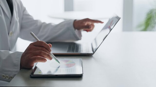 ノートパソコンとタブレットPCを使って作業する白衣の男性。科学、研究、医療、医師、実験、データ、分析