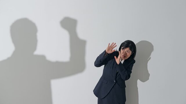 男性のシルエットに叩かれる女性ビジネスパーソン。パワハラ、カスハラ、殴る、上司、DV、企業、圧力