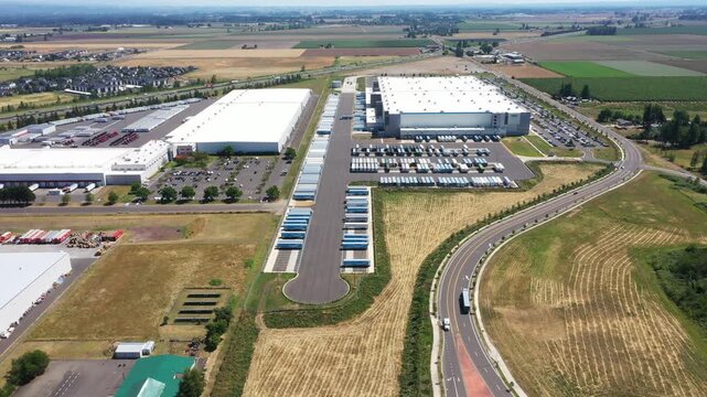 4K aerial drone footage of a major ecommerce fulfillment center and grocery distribution warehouses in Woodburn, Oregon, USA with numerous semi trucks, loading docks, and logistics operations