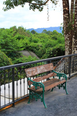 Fototapeta premium A weathered wooden bench sits quietly on a balcony, offering a peaceful spot to rest and enjoy the lush green forest view and the distant blue mountains.