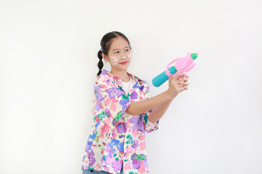 Portrait of young Asian girl with white powder on her cheeks enjoys the Songkran festival, aiming her water gun and smiling while wearing vibrant floral summer shirt.
