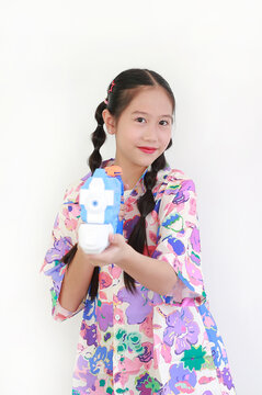 Smiling young Asian girl in colorful floral shirt posing with water gun against white background, ready for Songkran festival fun.
