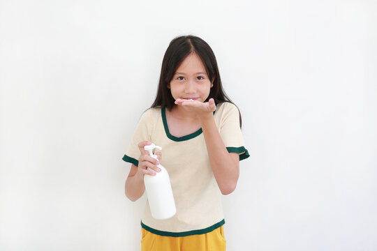 Asian girl is smiling at camera and demonstrating the use of a pump dispenser bottle to apply lotion or moisturizer to her hands, set against white background.