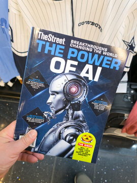 CHICAGO, IL, USA - JANUARY 20, 2026: A person holds 'TheStreet: The Power of AI' magazine against a backdrop of a Cowboys jersey. TheStreet is a leading financial news and services provider...