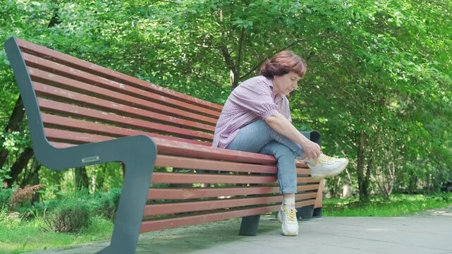 senior woman adjusting comfortable shoes on park bench before long walk. orthopedic shoes provide support for elderly joints. proper shoes ensure safe and painless walking for senior woman today