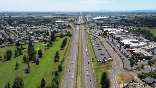 4K aerial drone video footage of Interstate 5 near Woodburn, Oregon, USA on a clear summer day, featuring traffic flow, surrounding commercial district, green spaces,  a popular outlet shopping center