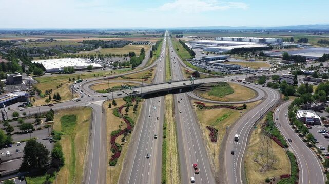 4K aerial drone static footage of Interstate 5 interchange near Woodburn, Oregon, USA with busy summer traffic, highway ramps, overpass, and surrounding commercial and industrial development.