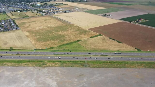 4K static aerial drone footage of Interstate 5 near Woodburn, Oregon, USA showing busy summer traffic from a side angle with surrounding farmland, agricultural fields, and residential development