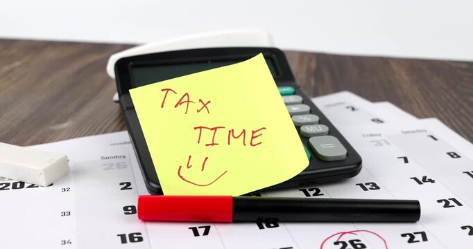 Horizontal panning view of financial tax time concept featuring an office calendar with stickynote and electronic calculator tool