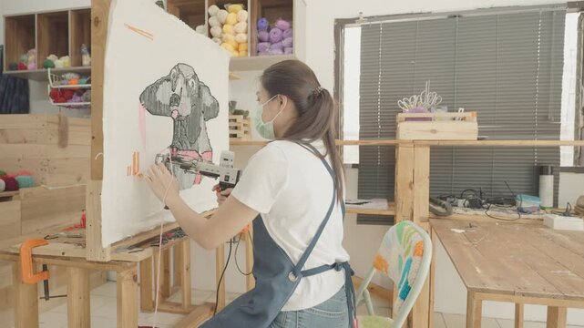 A detailed view of an artist at work in a craft studio, showcasing the intricate needlework of a colorful design. The workspace is filled with materials, providing a glimpse into the creative process.
