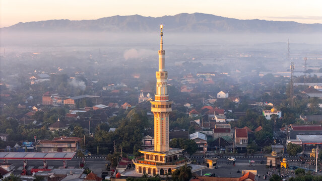 Kecamatan Klaten Utara, Indonesia - 02 July 2026: Aerial view of Al Aqsha Great Mosque Klaten with its tall minaret rising above urban rooftops and misty mountains in the soft morning light.