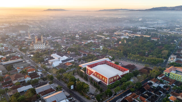 Kecamatan Klaten Utara, Indonesia - 02 July 2026: Aerial view of GOR Gelarsena Klaten surrounded by urban residential areas, a mosque, and greenery under soft morning light.