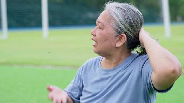 Asian elderly man outdoors expressing discomfort in hot weather, symbolizing heat wave, El Ni&ntilde;o, climate change, wellness, and lifestyle impact in natural environment with greenery and daylight