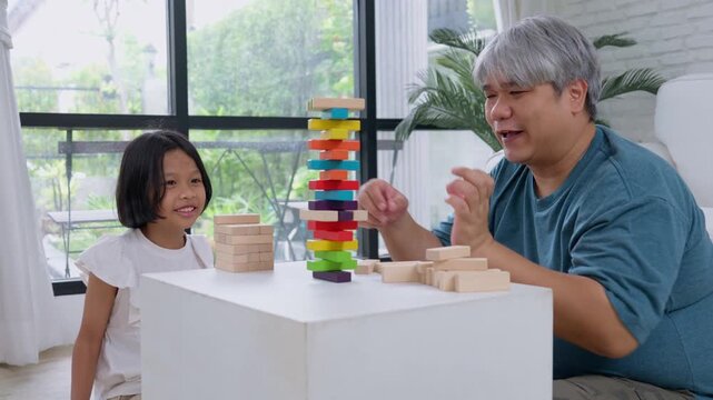Asian girl child playing stacking game with father, symbolizing family bonding, education and childhood development in cheerful home environment with learning concept, positive atmosphere