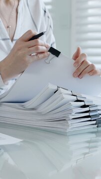 Person's hands meticulously reviewing and organizing extensive business documents and financial reports fastened with binder clips. Illustrating the demanding nature of administrative work