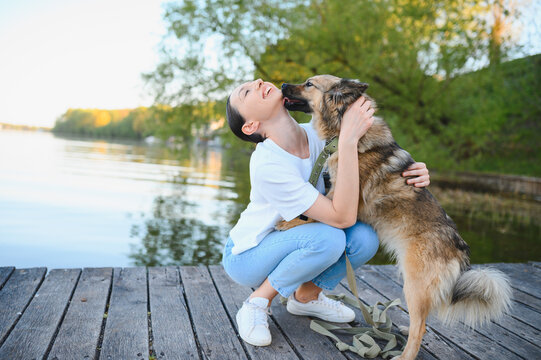 Woman embracing dog receiving affectionate lick on dock