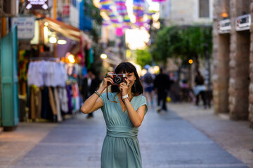 Fototapeta premium Close-up of a dark-haired woman holding a vintage camera near her face, looking through the viewfinder with focused expression.