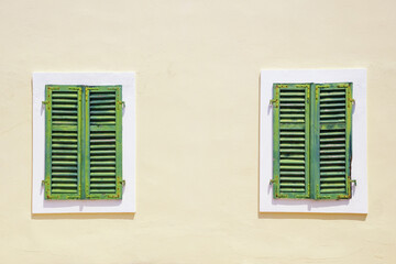 Fototapeta premium Building facade with two windows covered with old green wooden shutters. Copy space