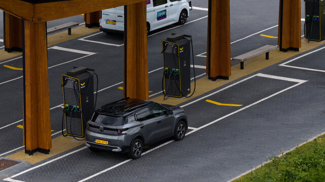 Muiden, Netherlands - 11 June 2026: Aerial view of the Fastned charging station with a grey car parked at a charging point, featuring wooden pillars and modern EV infrastructure.