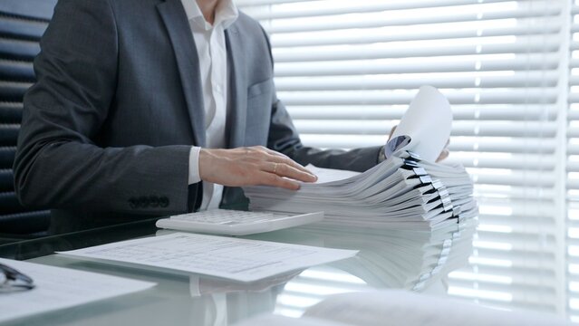 Businessman's hands are busy managing and organizing a large stack of financial papers and business documents